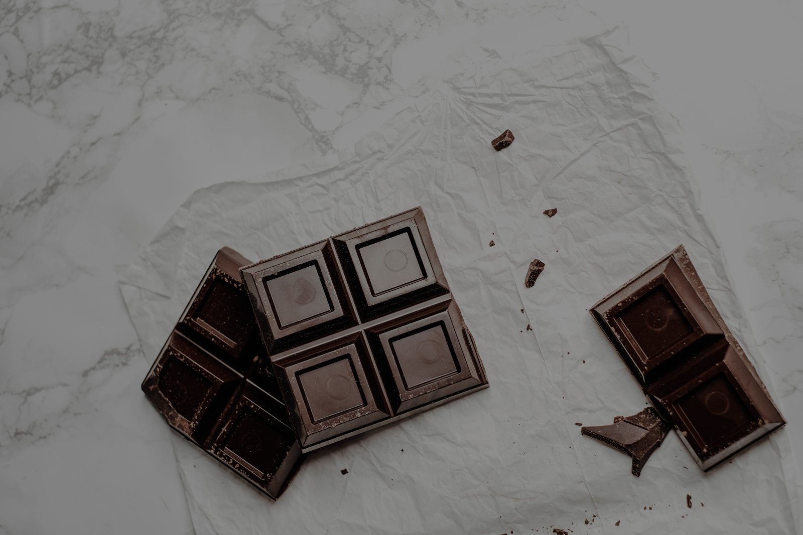 A part-eaten bar of dark chocolate broken into squares on white marble.