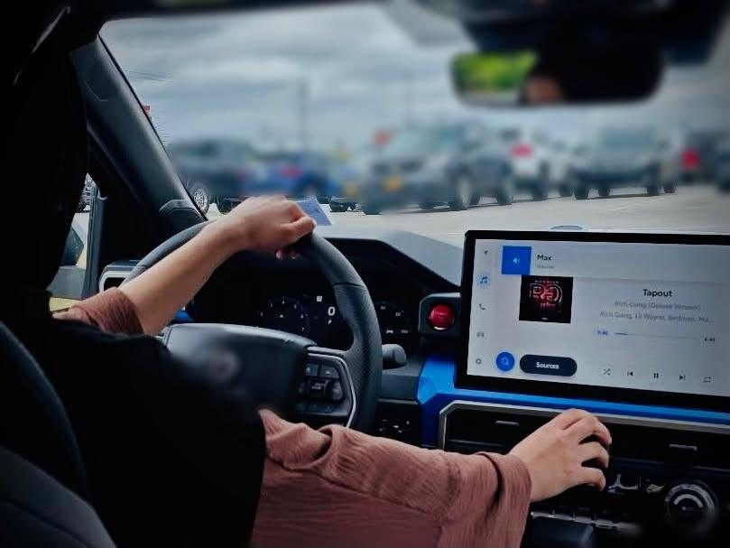 A driver’s hands on the wheel and on the touchscreen of a car in slow traffic.