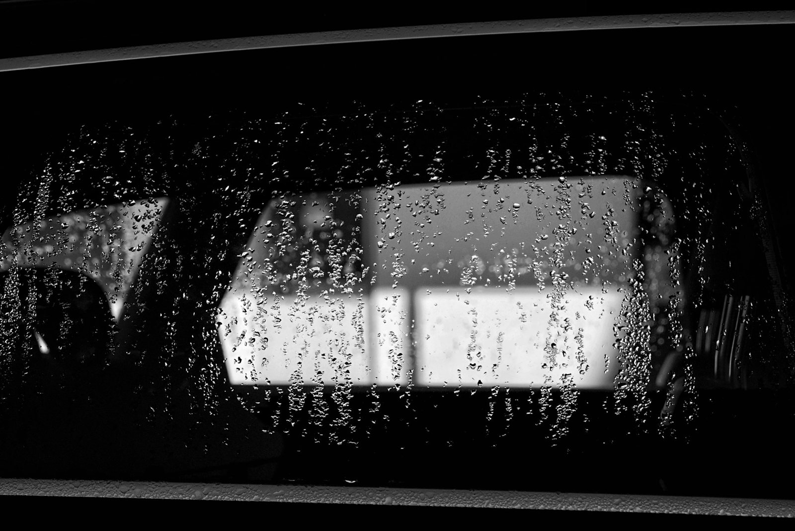 Rain on a car window at night, lit windows blurred beyond the glass.