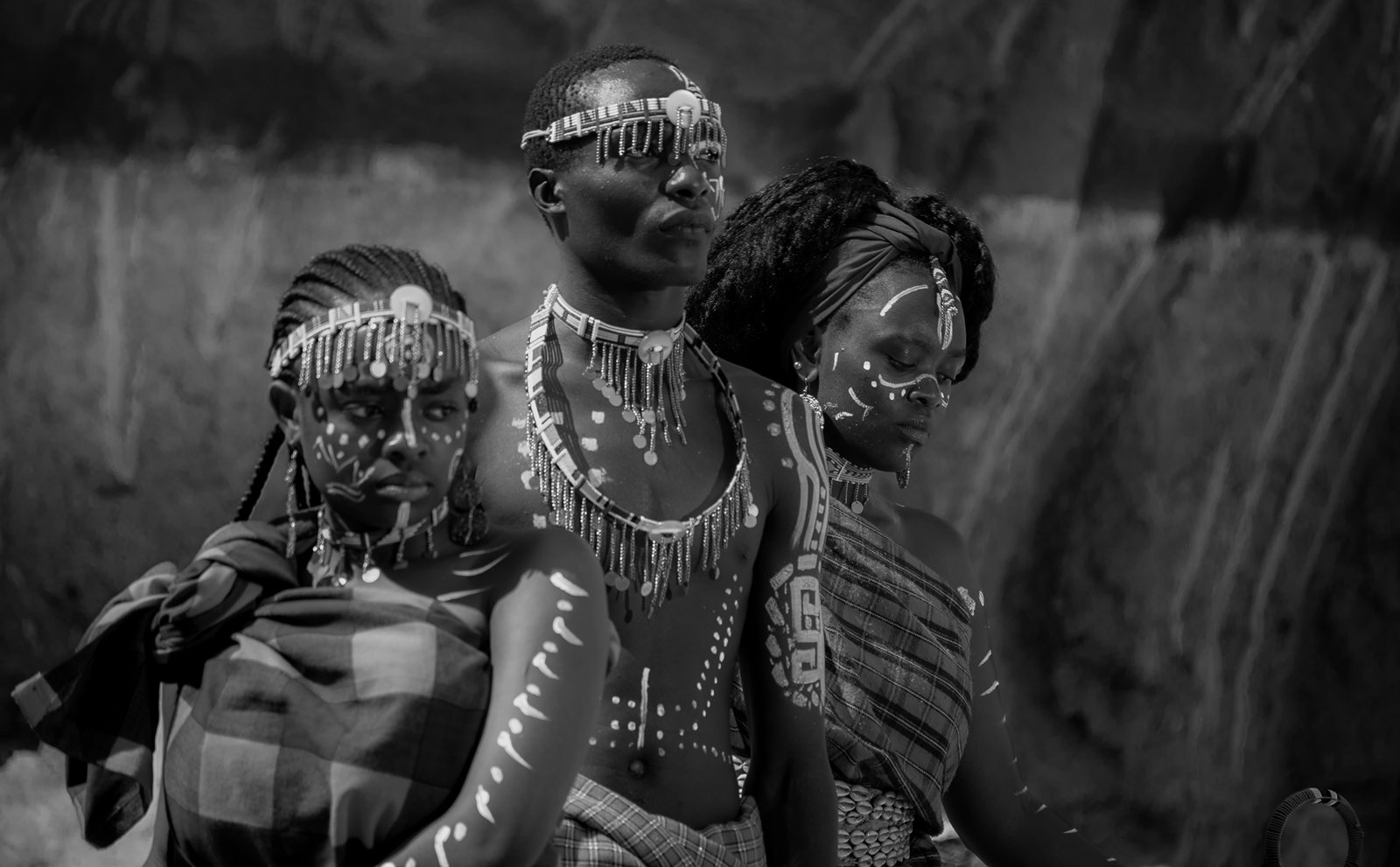 A black-and-white photograph of three people in elaborate beaded headdresses and necklaces.