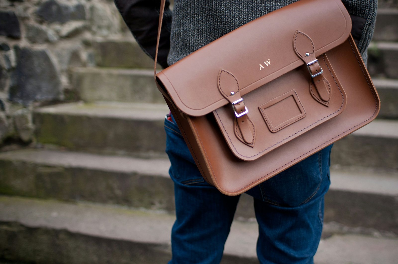 A person on stone steps carrying a tan leather satchel.