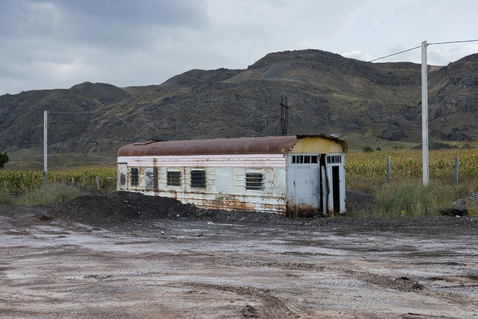 An abandoned single-storey building beside a dirt road under bare hills.