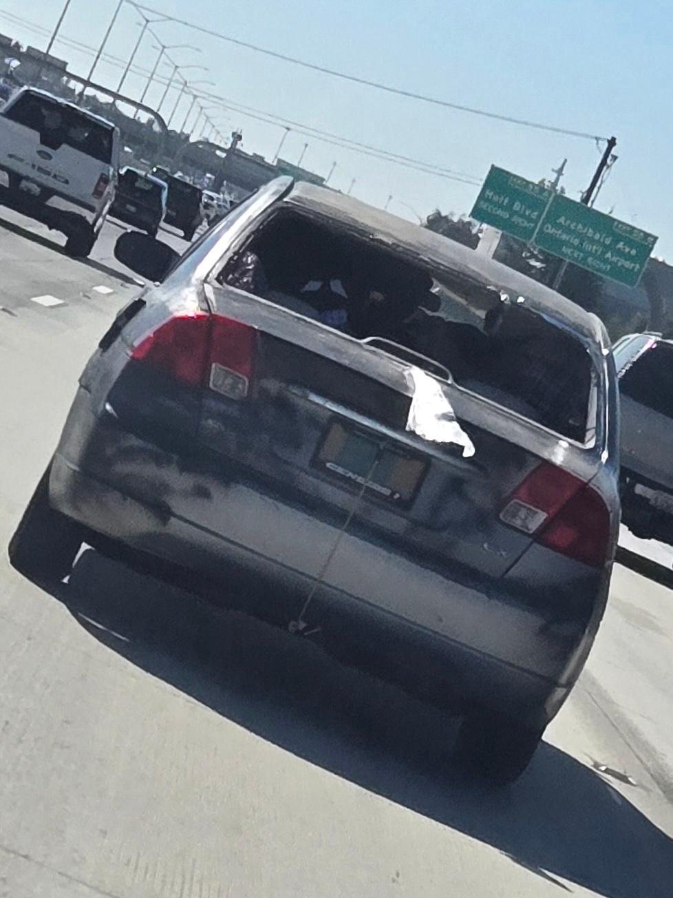 The back of a parked car in traffic, seen through a windscreen.