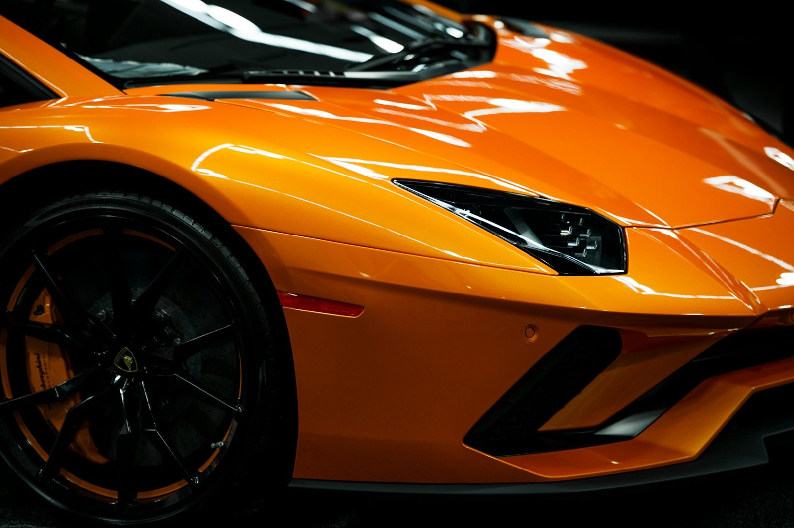 The front wheel and headlight of a bright orange sports car, close in.
