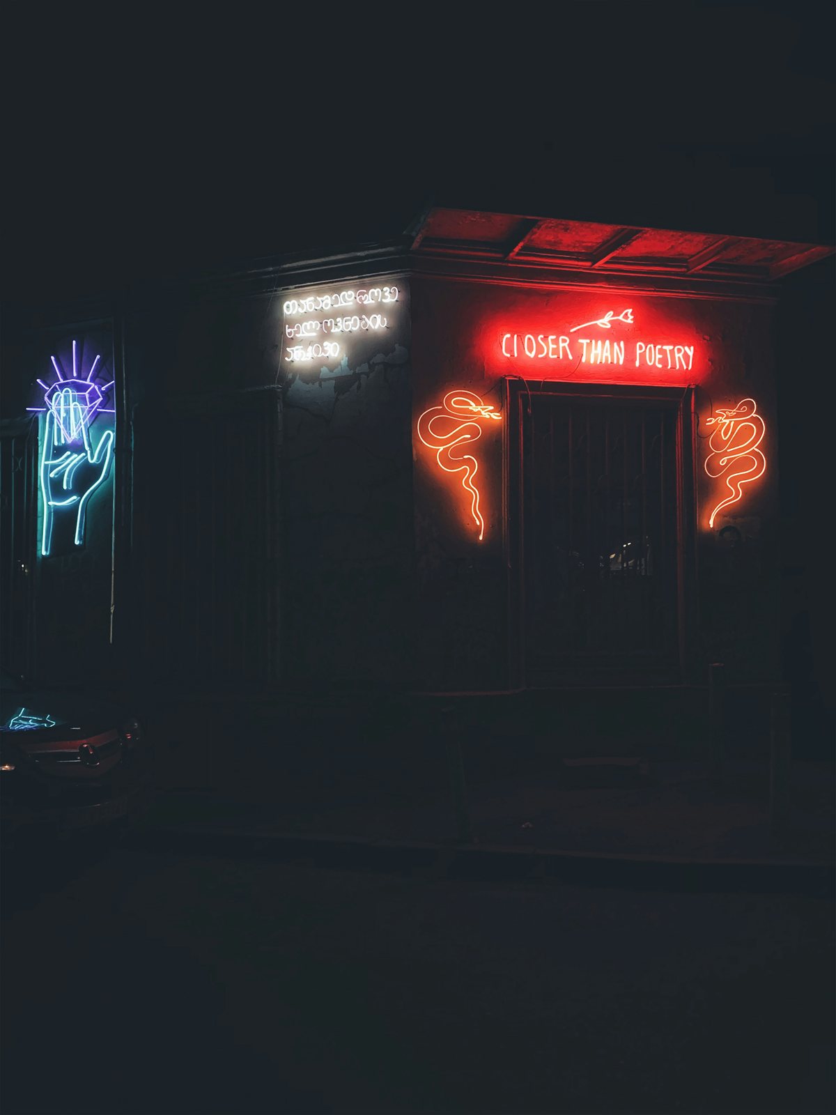 A bar front at night under red and blue neon signs.