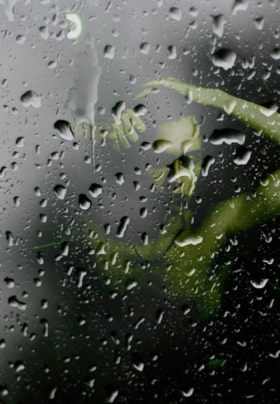 A rain-streaked window with a blurred green figure behind the glass.