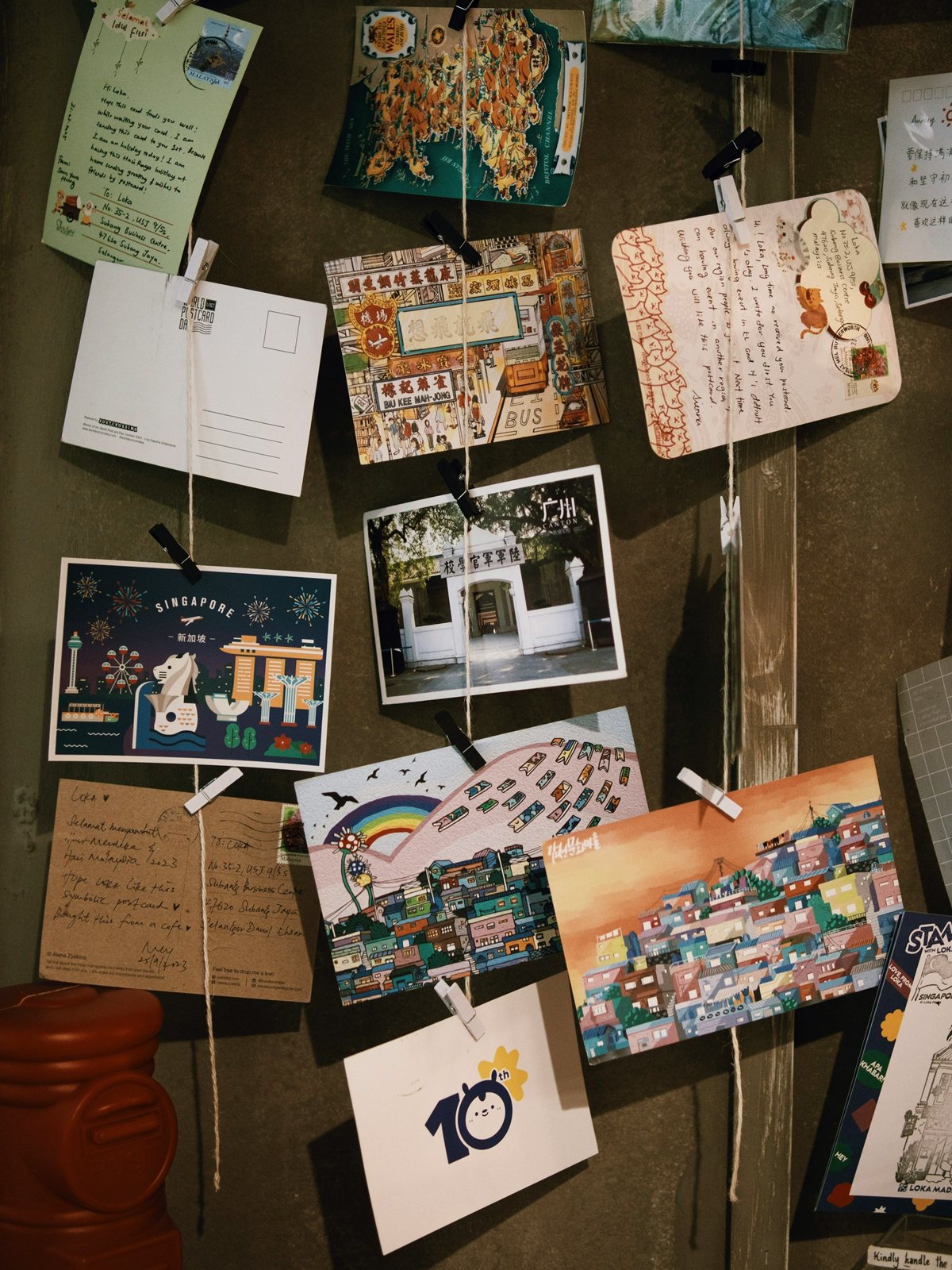 A noticeboard crowded with postcards, photographs and handwritten notes.