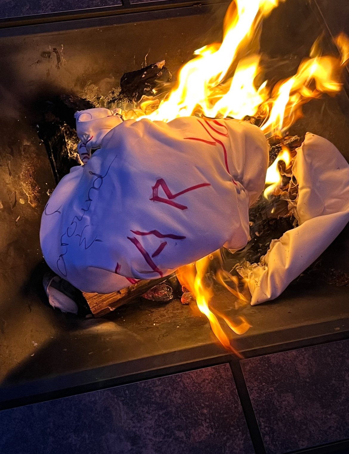 A white garment marked with red writing, burning on a tiled surface.