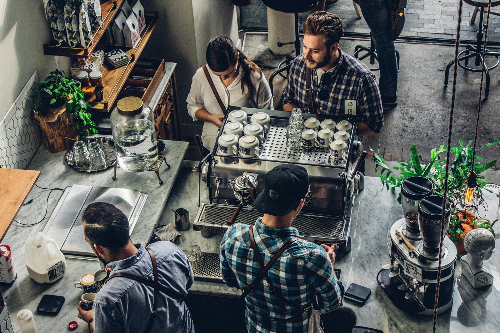 Looking down on a busy café counter, staff at the espresso machine and customers along the bar.