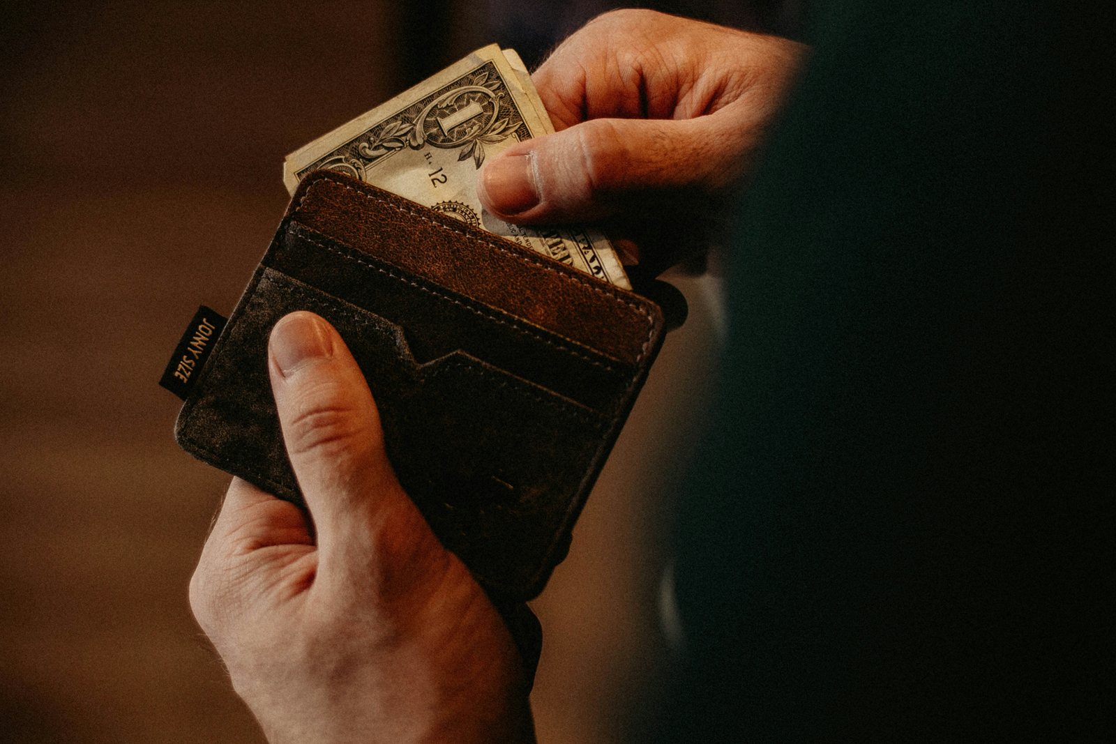 A hand drawing banknotes out of a worn leather wallet.