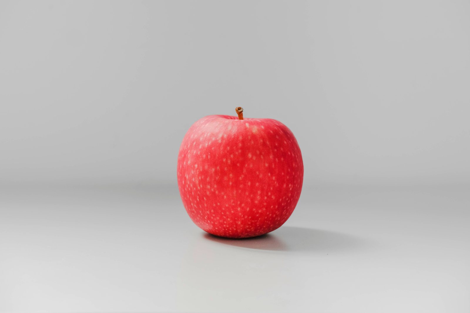 A single red apple on a plain pale ground.